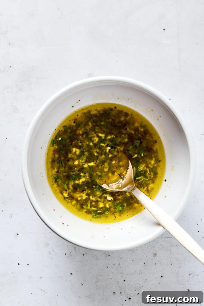 Fresh, flavorful Lemon Chicken is incredibly easy to make, and totally mouthwatering, too! Black pepper, garlic, fresh herbs, and lemon. Yum! Mixing marinade ingredients in a bowl with a whisk.