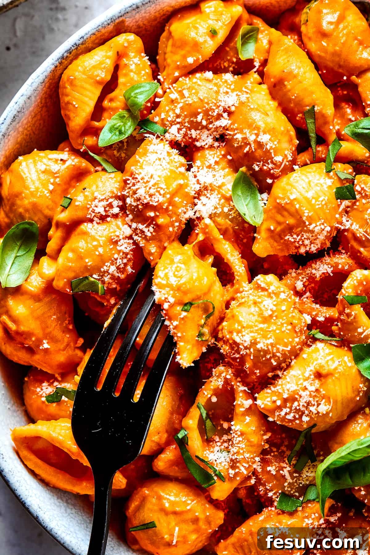 A fork in a bowl of Gigi Hadid pasta, garnished with fresh basil.