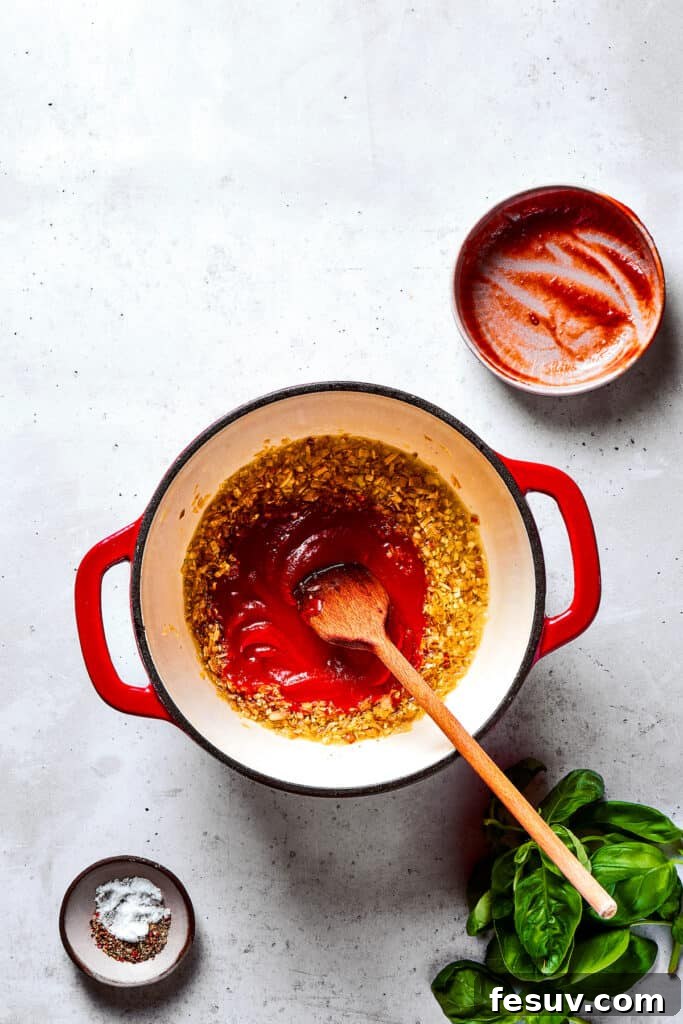 Tomato paste being sautéed with aromatics in a pan, deepening its flavor.