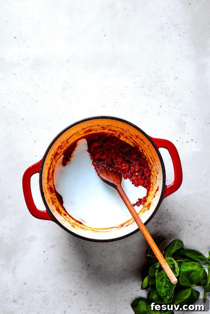 Gently stirring heavy cream into the simmering tomato sauce, creating a rich and vibrant base.
