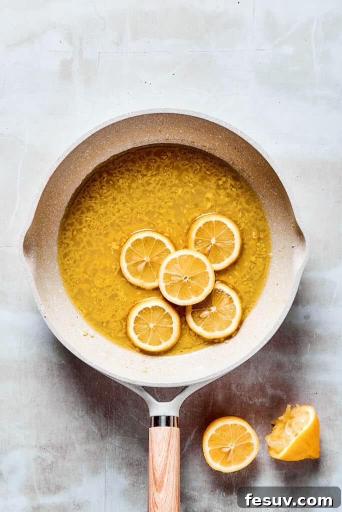 The final touch: Sliced lemons added to the rich sauce for Lemon Chicken. Thinly sliced lemons are added to the simmering sauce in a skillet, infusing it with fresh citrus flavor.