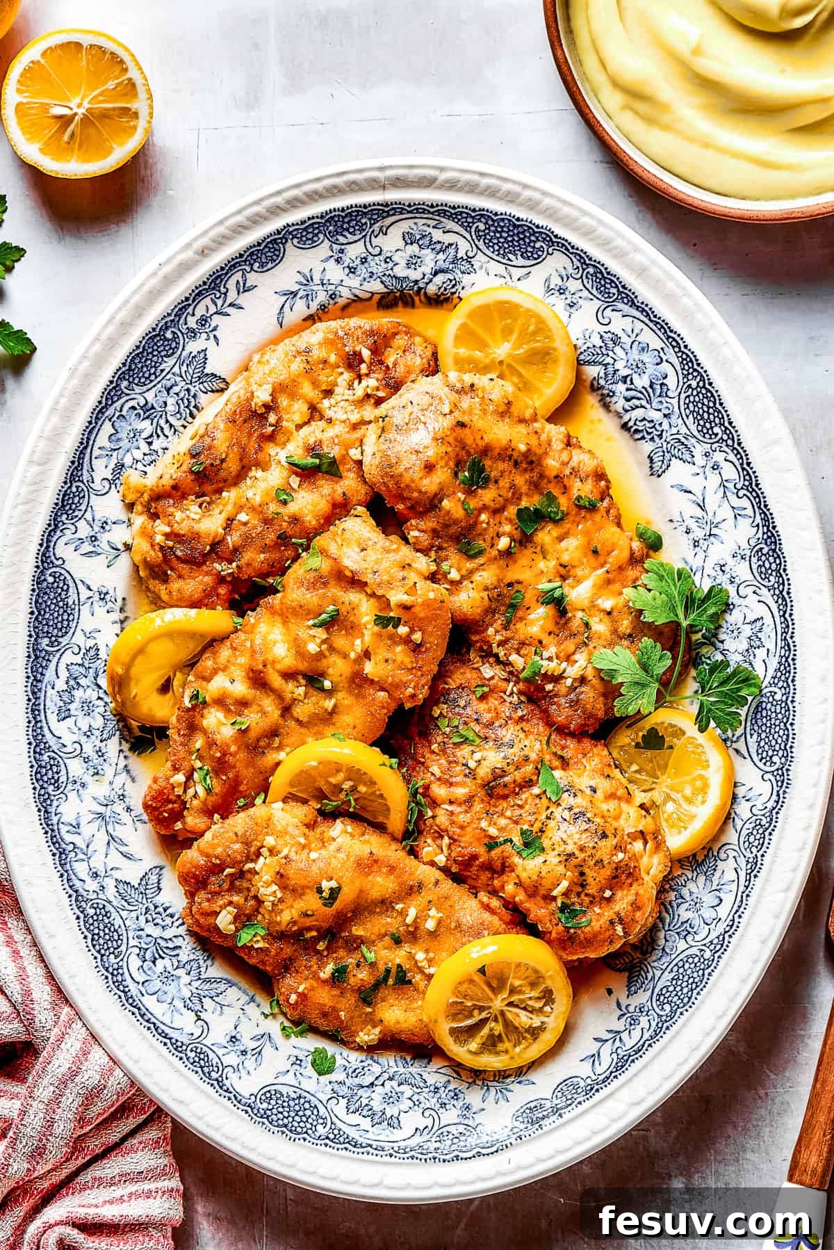 A beautifully presented Lemon Chicken Recipe: Crispy, parmesan-crusted chicken with real lemon butter sauce. Perfectly cooked lemon chicken breasts arranged elegantly on a stylish blue oval plate, garnished with fresh herbs and lemon wedges.