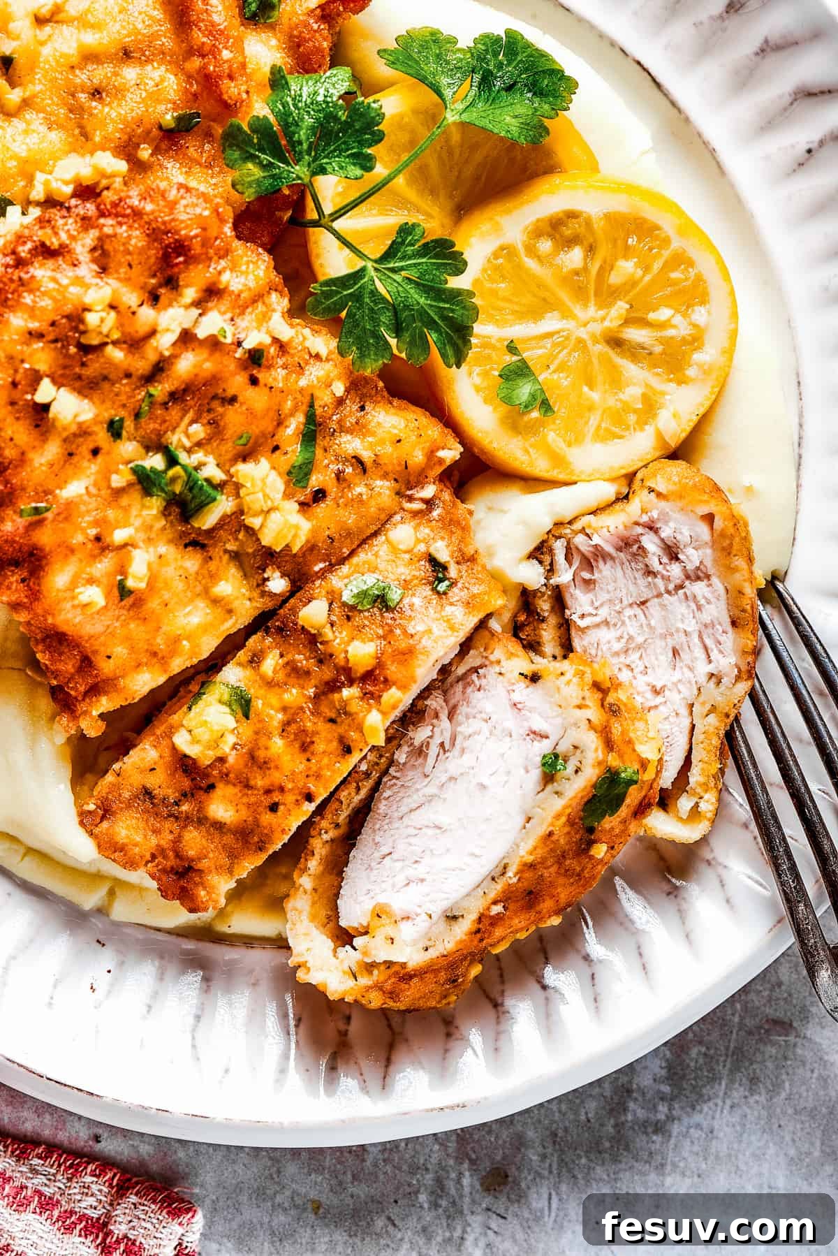 Enjoying a delicious Lemon Chicken Recipe: Crispy, parmesan-crusted chicken with a real lemon butter sauce. Yum! Sliced breaded chicken served on a plate, garnished with fresh parsley and vibrant lemon slices.