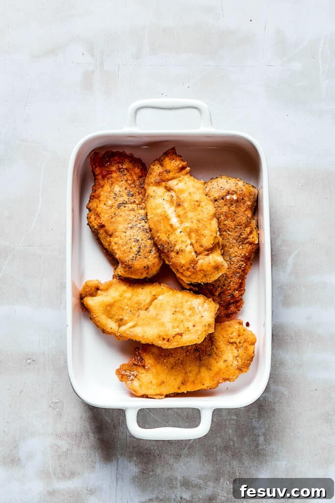 Baked to perfection: Lemon Chicken with crispy, parmesan-crusted chicken in real lemon butter sauce. Golden-brown, breaded chicken breasts neatly arranged in a baking dish, ready for the oven.