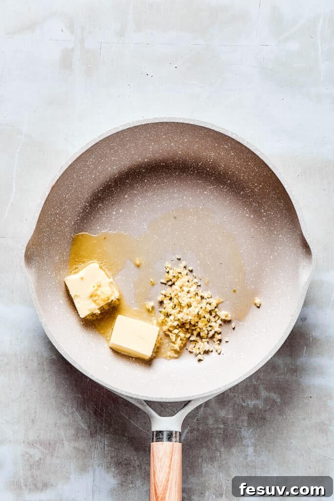 The savory base for our Lemon Chicken sauce: Crispy, parmesan-crusted chicken with real lemon butter sauce. Minced garlic sizzling in melted butter in a skillet, creating a fragrant base for the sauce.