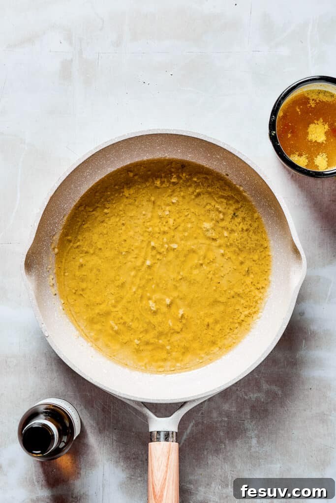 Creating the flavorful sauce for Lemon Chicken: Crispy, parmesan-crusted chicken with real lemon butter sauce. Chicken broth and dry white wine being poured into a hot skillet, deglazing the pan and forming the sauce base.