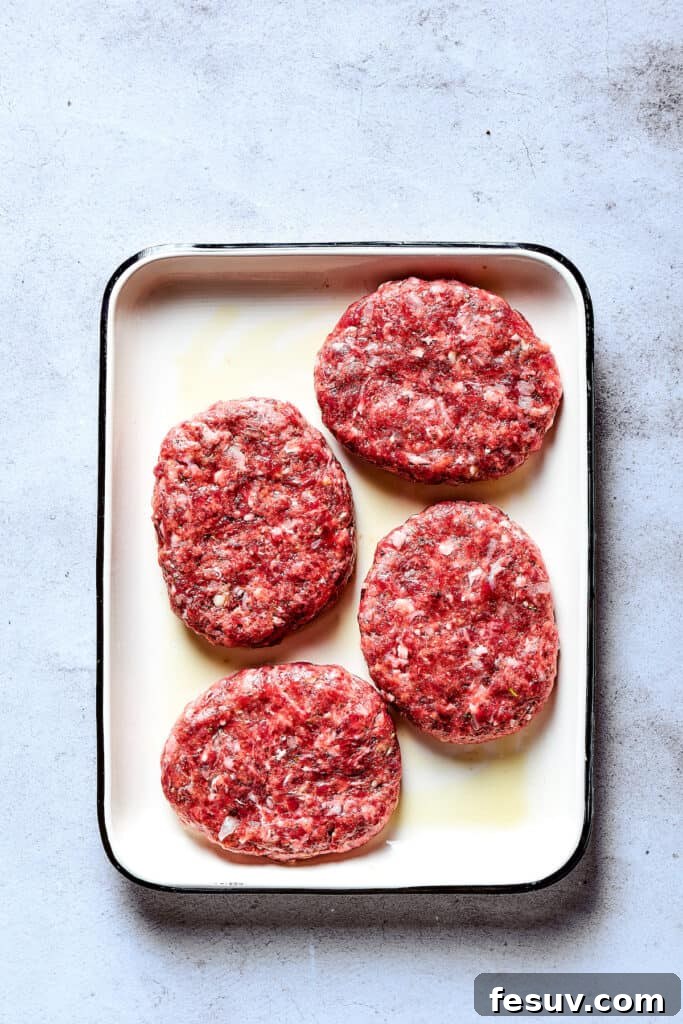 Six evenly shaped beef patties, oval in form, are arranged on an enamel tray, ready for cooking.