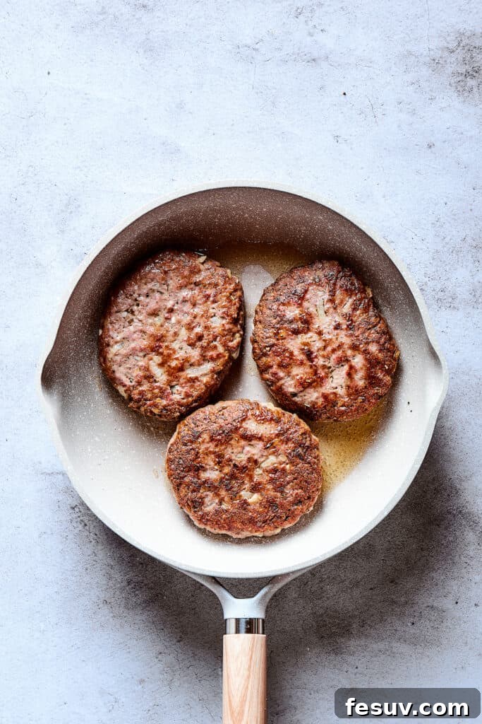 Several beef patties are shown sizzling and browning in a hot skillet, developing a delicious crust before being removed to make way for the gravy.