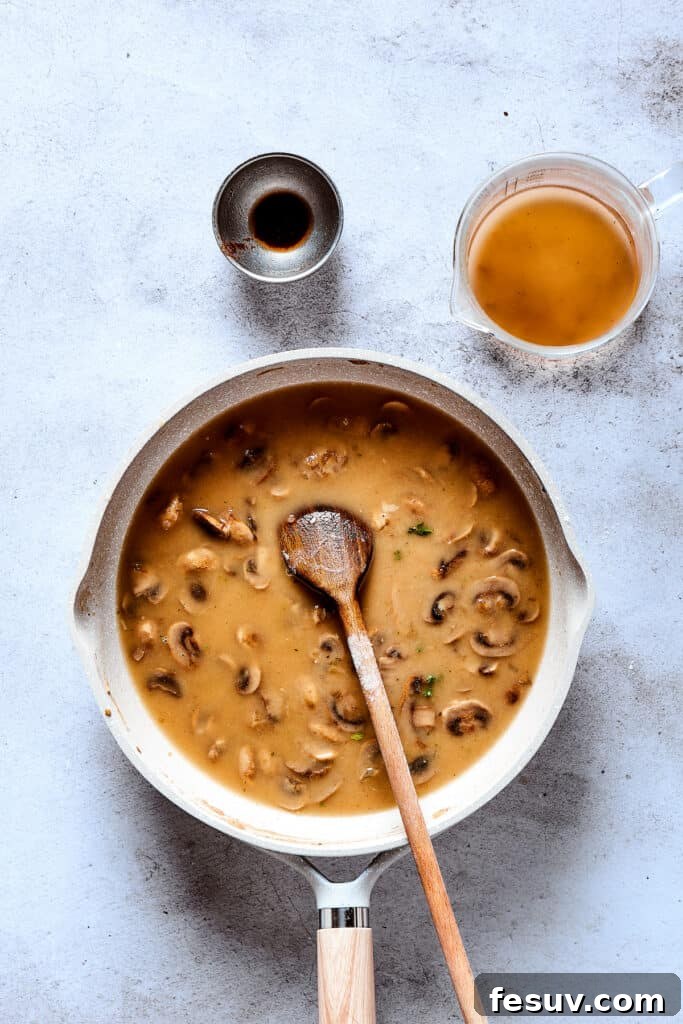 A rich, bubbling mushroom gravy is shown in a skillet, thickened to perfection and ready to receive the Salisbury steak patties.