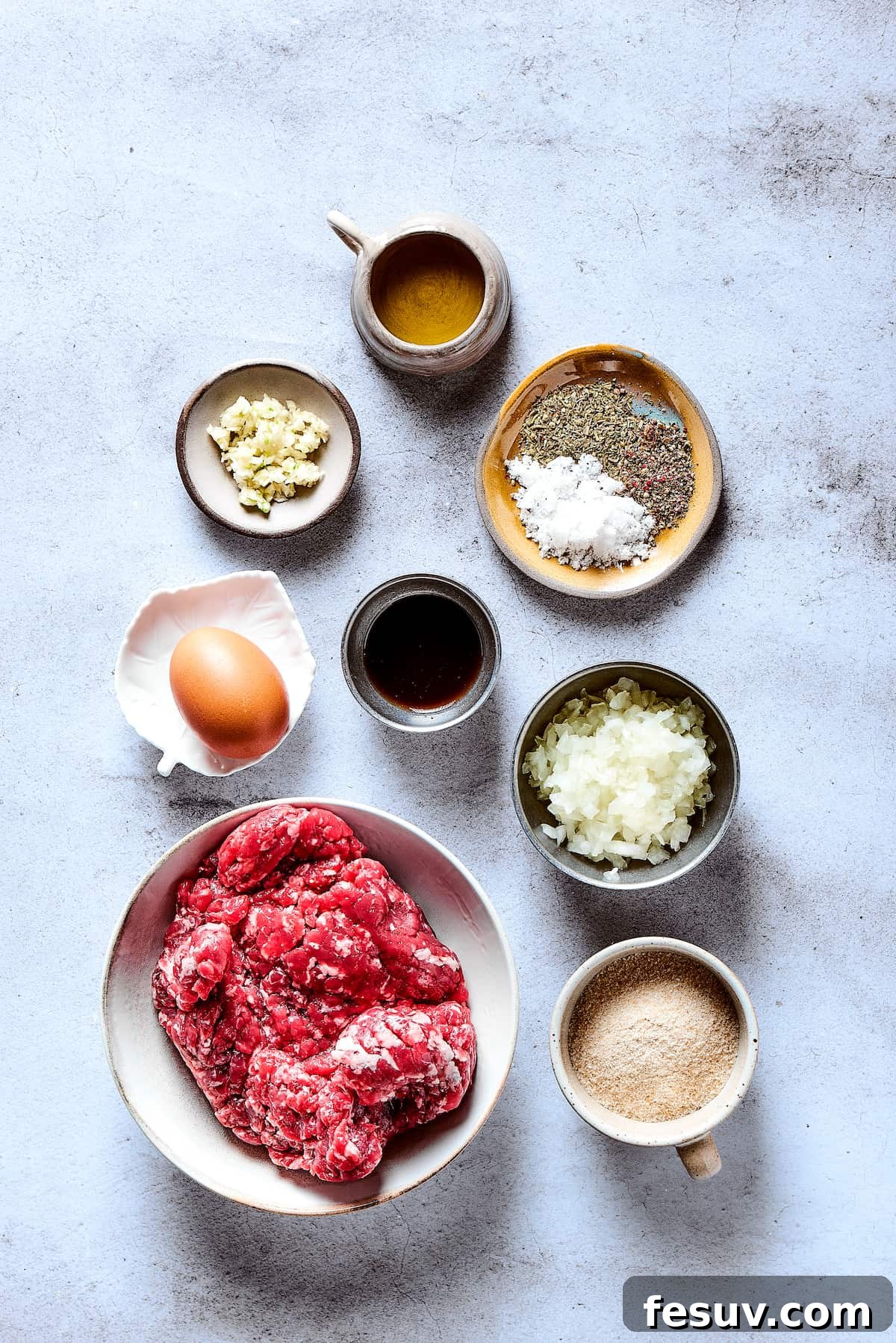 A vibrant array of fresh ingredients for Salisbury steak, including ground beef, eggs, onions, garlic, breadcrumbs, and various seasonings, all neatly arranged on a clean wooden work surface, ready for preparation.