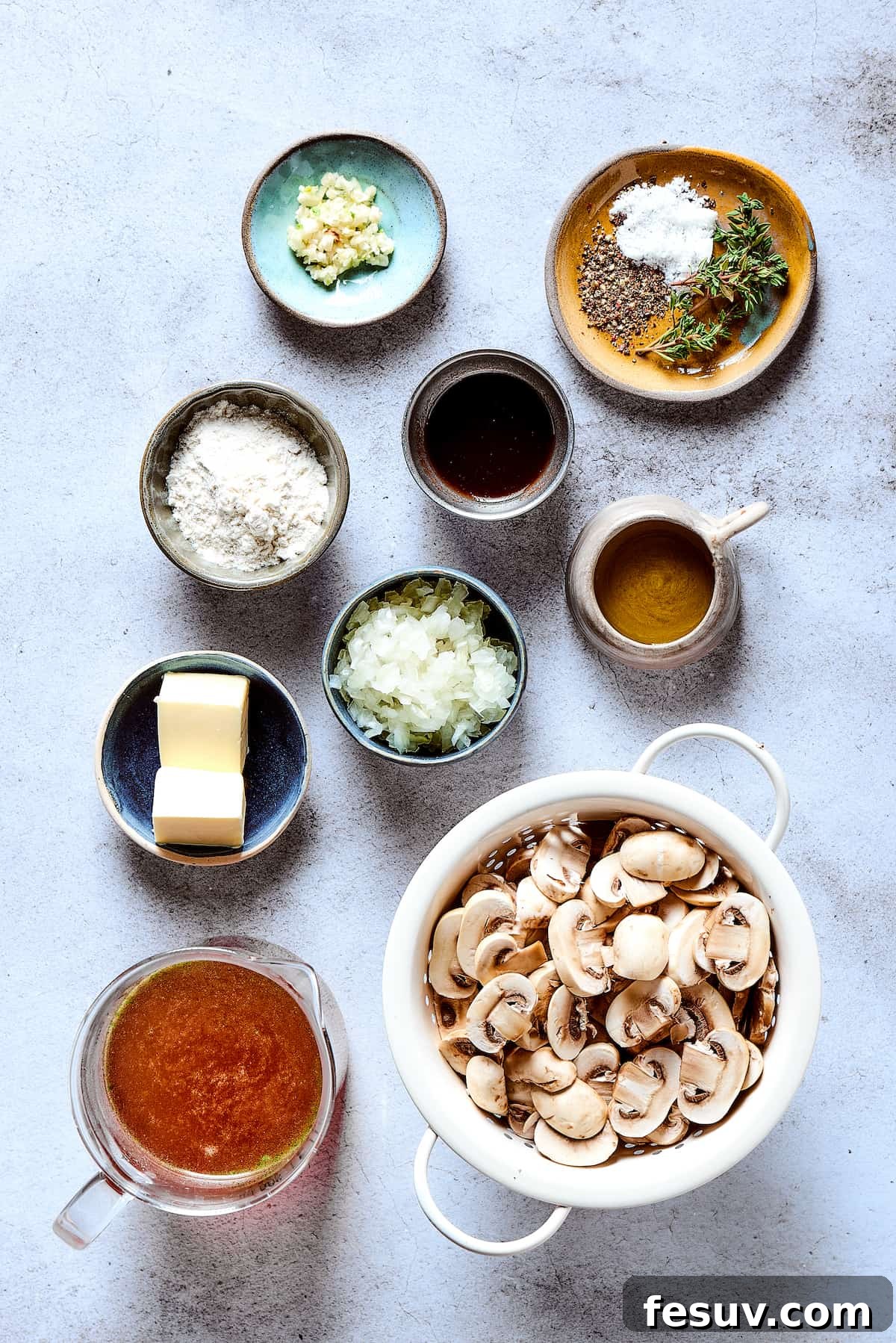 A collection of fresh ingredients for mushroom gravy, including sliced mushrooms, chopped onions, fresh thyme, beef broth, butter, and olive oil, neatly laid out on a clean work surface, ready for preparing the rich sauce.