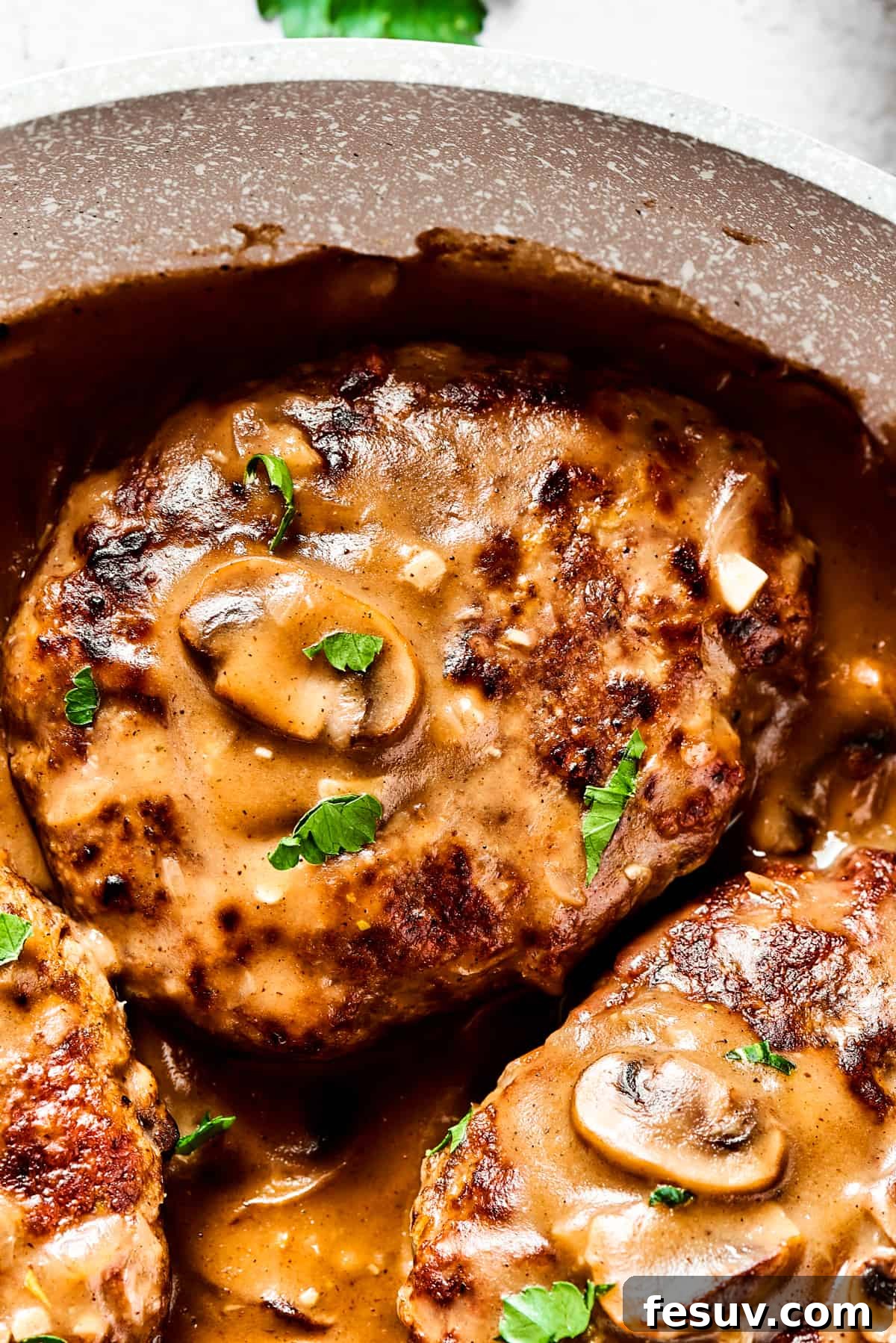 A close-up view of a single Salisbury steak, generously topped with an abundance of sautéed mushrooms and a thick, glossy mushroom gravy, showcasing the appetizing texture and richness of the dish.