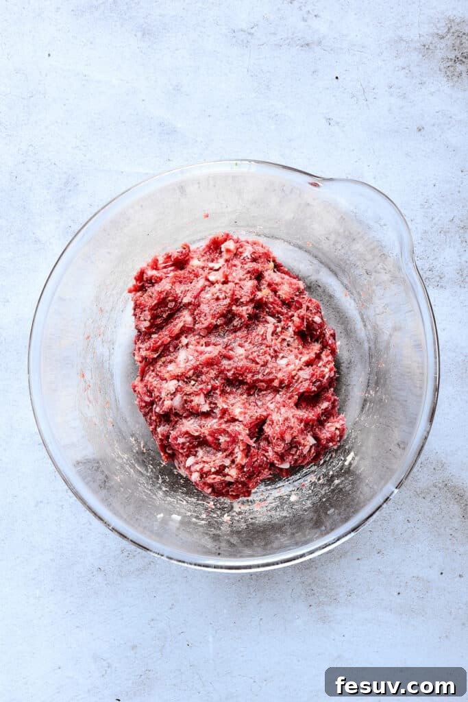 The thoroughly mixed ground beef patty mixture, incorporating onion, breadcrumbs, egg, and seasonings, is shown in a clear glass dish, ready for shaping.