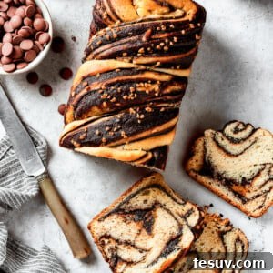 A loaf of chocolate babka that has been partially sliced. The slices are laid out on the work surface along with a bread knife and a dish of chocolate chips.