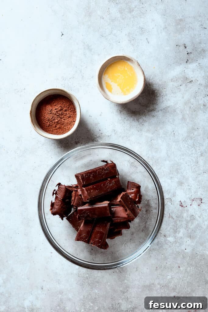 Chocolate in a glass bowl next to a dish of melted butter and a dish of cocoa powder.