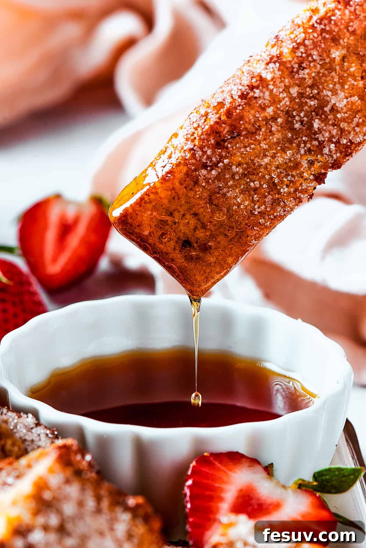 Lifting a piece of toast from a cup of syrup, with the syrup dripping back into the cup.