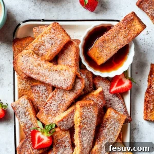 A tray of French toast sticks with maple syrup and strawberries. One stick is dunked in the syrup.