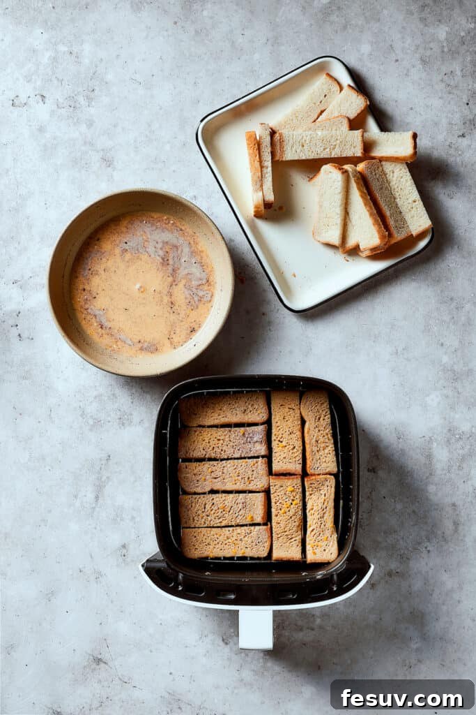 Custard-soaked bread sticks lined up neatly in an air fryer. Additional bread and custard are nearby.