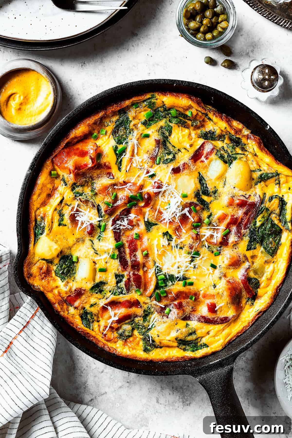 Spinach, Bacon, and Potato Frittata is a healthy, farmhouse-style dinner that's easy to make, and loaded with rich flavor. Perfect easy meal! overhead shot of a fully-cooked frittata in a cast-iron skillet.
