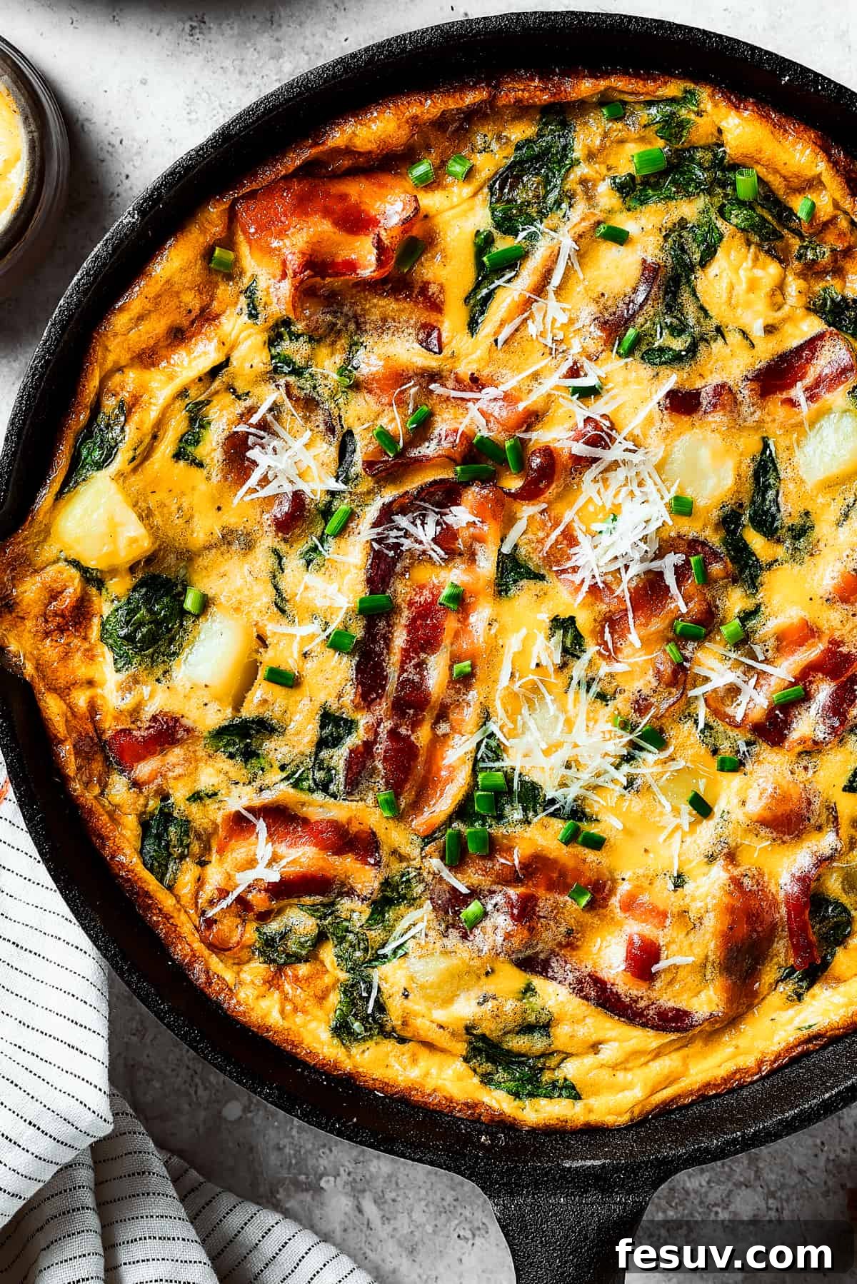 Spinach, Bacon, and Potato Frittata is a healthy, farmhouse-style dinner that's easy to make, and loaded with rich flavor. Perfect easy meal! Close-up overhead shot of a fully-cooked frittata in a cast-iron pan.