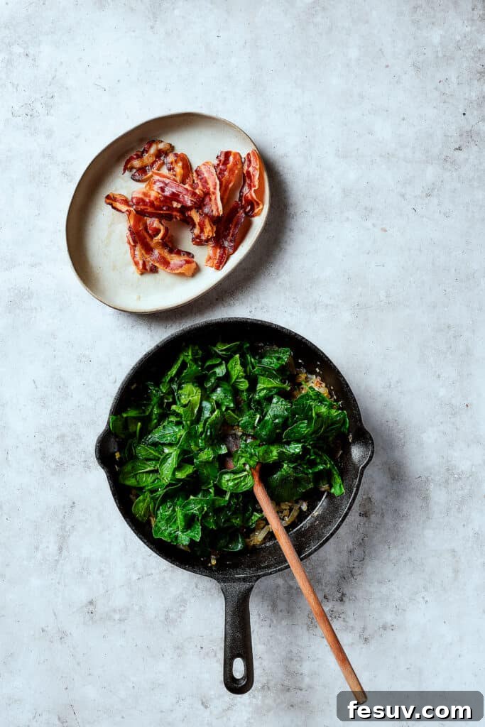 Spinach, Bacon, and Potato Frittata is a healthy, farmhouse-style dinner that's easy to make, and loaded with rich flavor. Perfect easy meal! Cooking spinach in a skillet with onion an garlic.