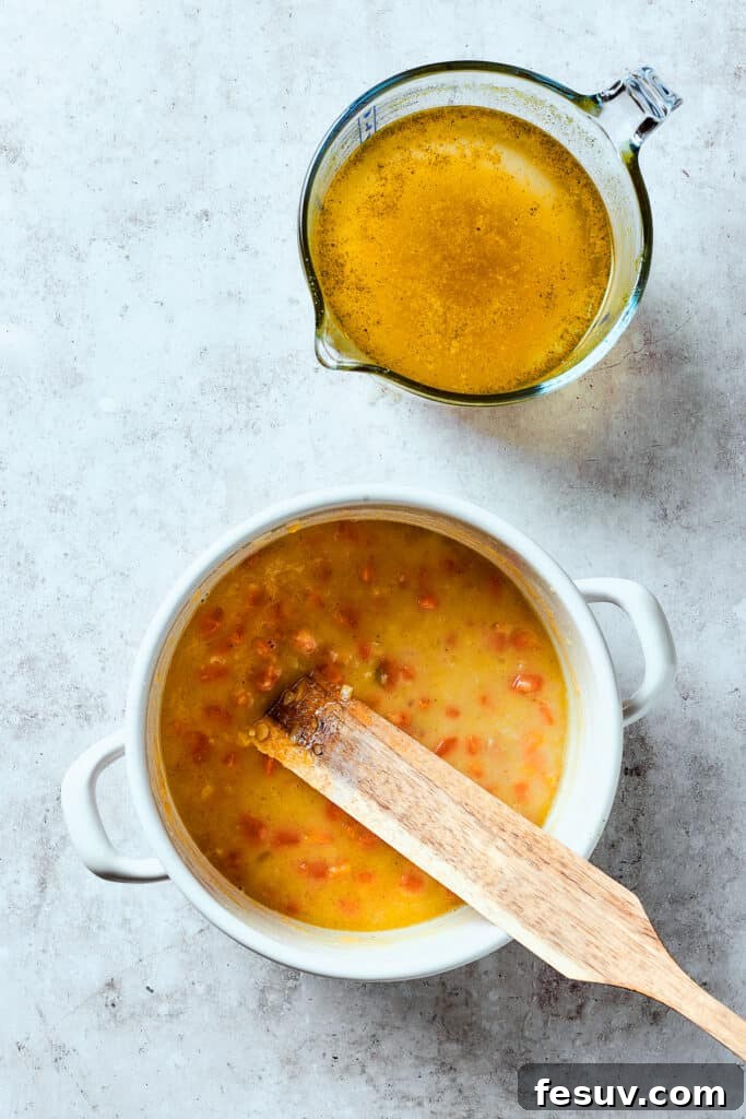 This Creamy Reuben Soup takes corned beef, sauerkraut, and Swiss to a whole new level! It's a comfy, cozy masterpiece in a bowl. Adding broth to a soup pot.