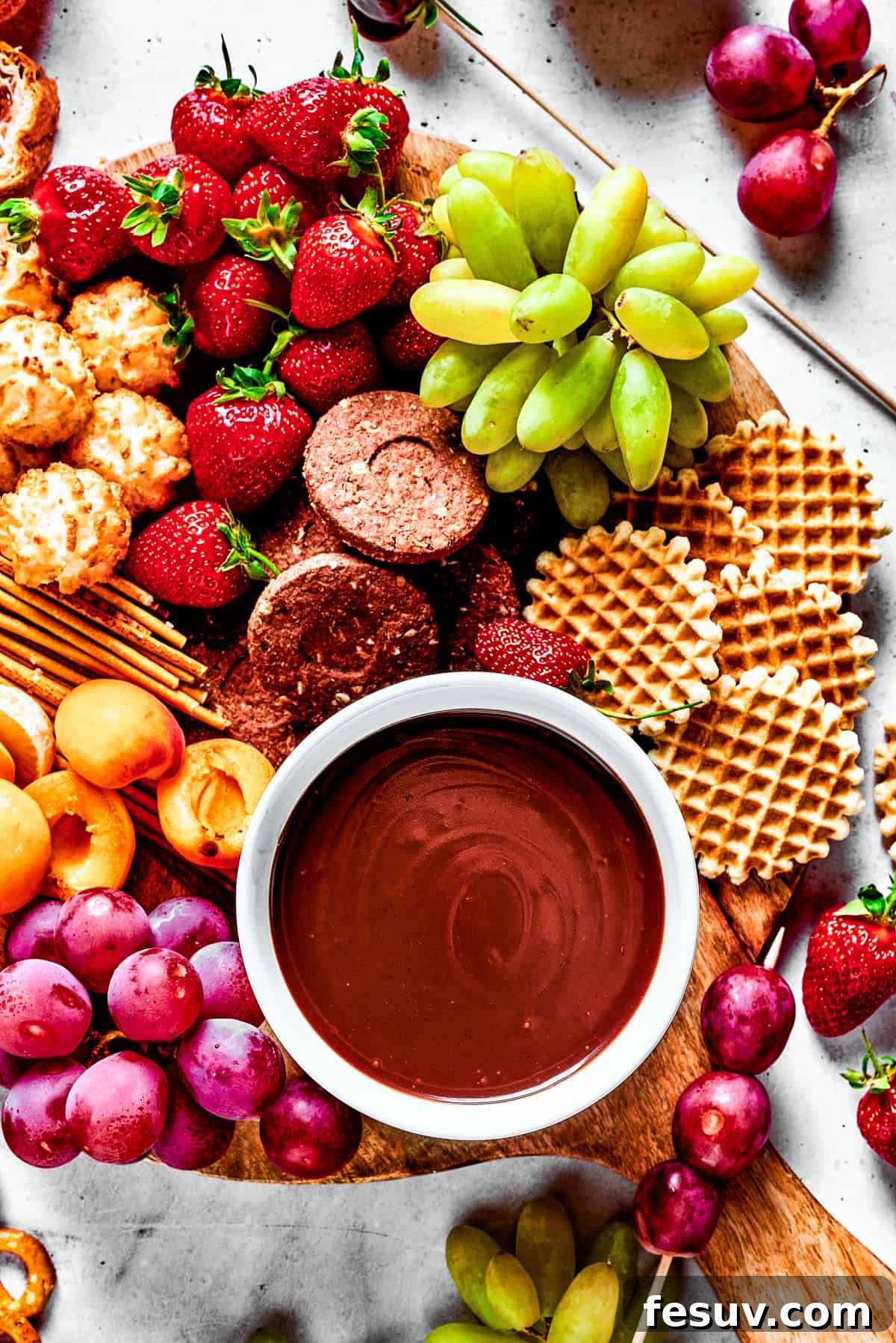 Velvet Chocolate Fondue 10 A dessert board with fruit, waffles, pretzels, and a bowl of fondue in the center.