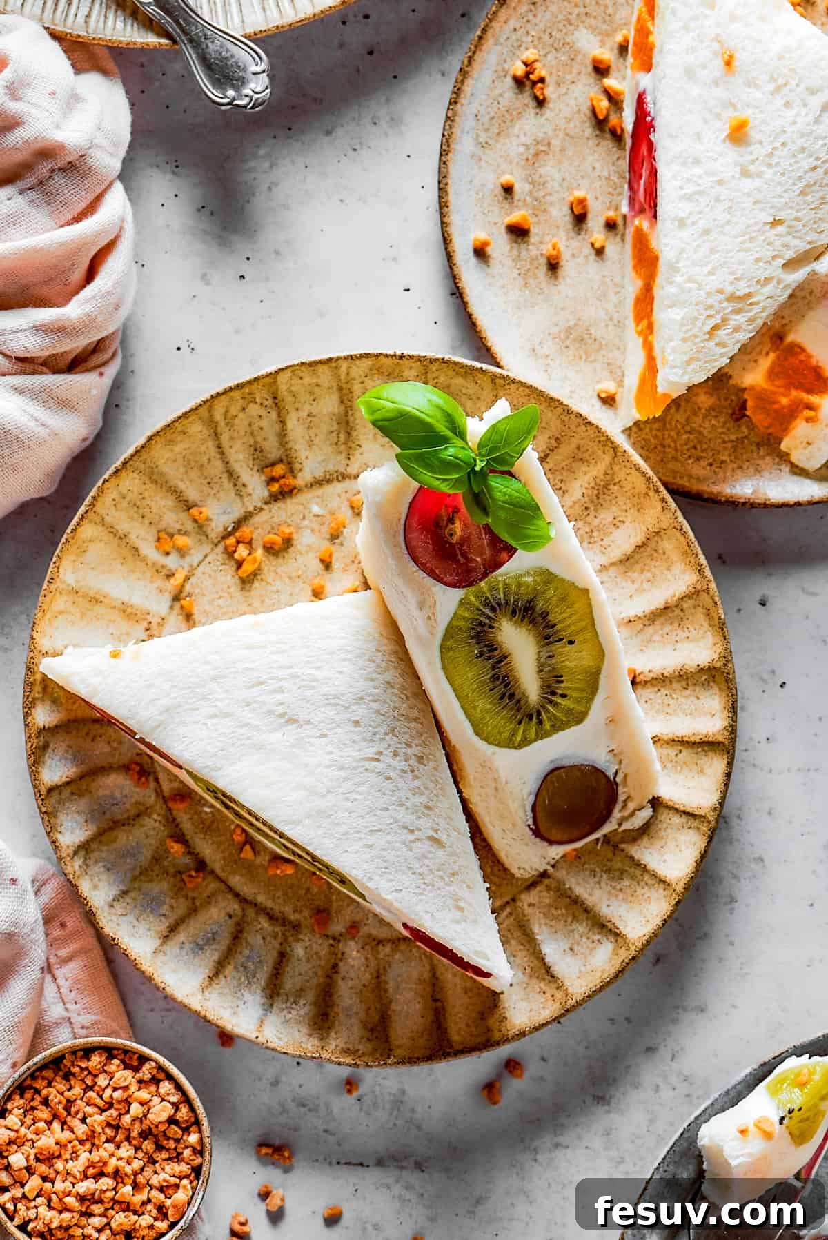 Overhead shot of fruit sandwich halves on a plate, showcasing a cross-section of colorful fruit and whipped cream.