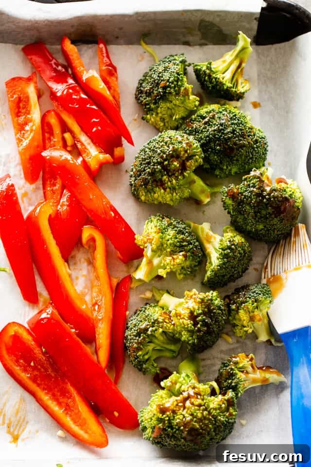 Enjoy a quick, flavorful meal with this sheet pan teriyaki shrimp stir fry, combining tangy sauce, crunchy veggies, and succulent shrimp. Red bell pepper slices and broccoli florets arranged on a baking sheet, ready for roasting.