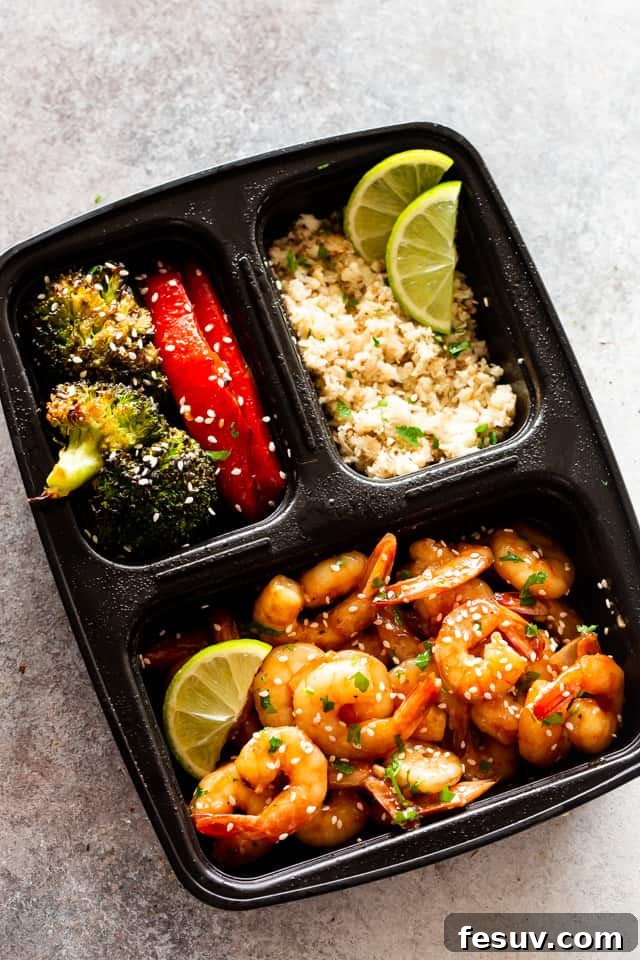 Enjoy a quick, flavorful meal with this sheet pan teriyaki shrimp stir fry, combining tangy sauce, crunchy veggies, and succulent shrimp. Photo of cooked shrimp, stir-fried veggies, and rice in a black meal prep container, ready for lunch.