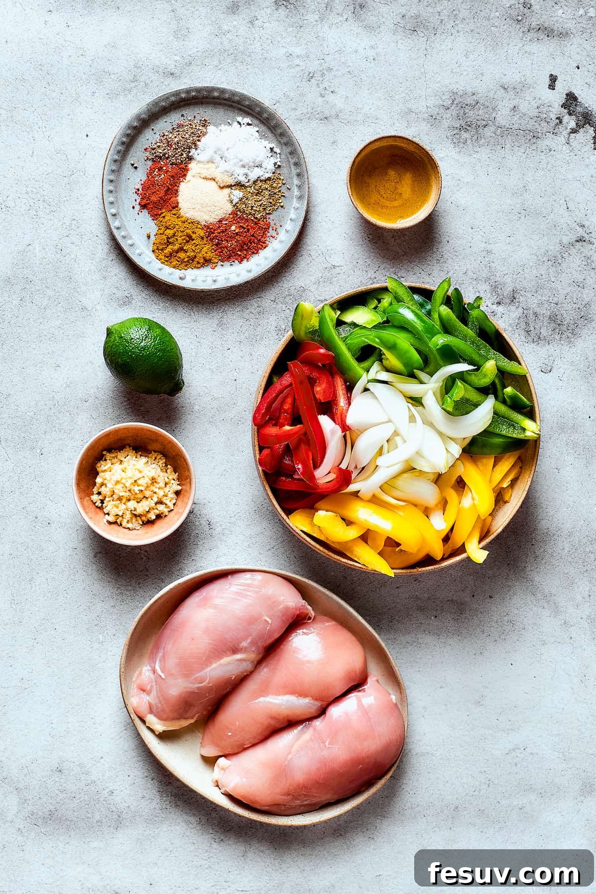 All the fresh ingredients for crockpot chicken fajitas, including chicken, bell peppers, onions, and spices, neatly arranged on a work surface.