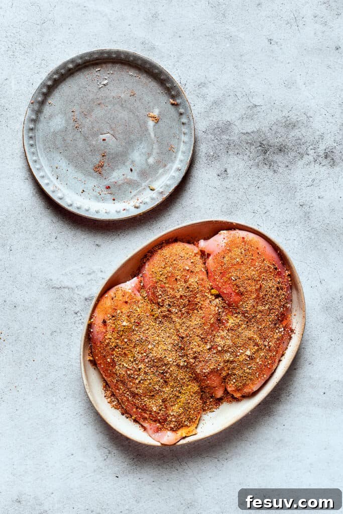 Seasoned chicken breasts on a plate, ready for the slow cooker.