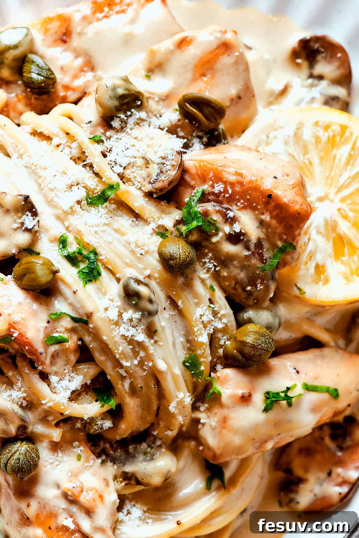 A close-up of the irresistible creamy chicken piccata pasta. Close-up shot of creamy pasta adorned with chicken piccata, bright capers, and fresh lemon slices, highlighting the rich texture of the sauce.