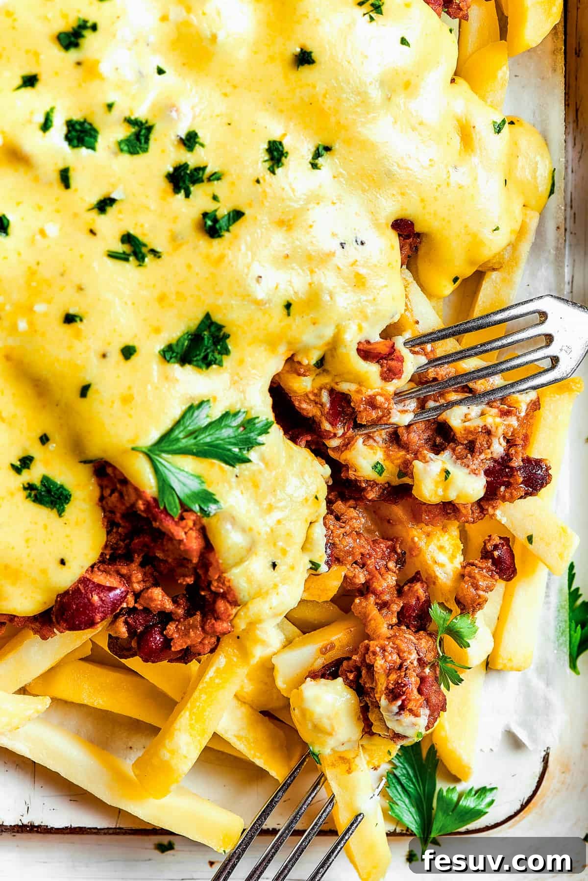 A fork taking a bite from a batch of chili cheese fries.
