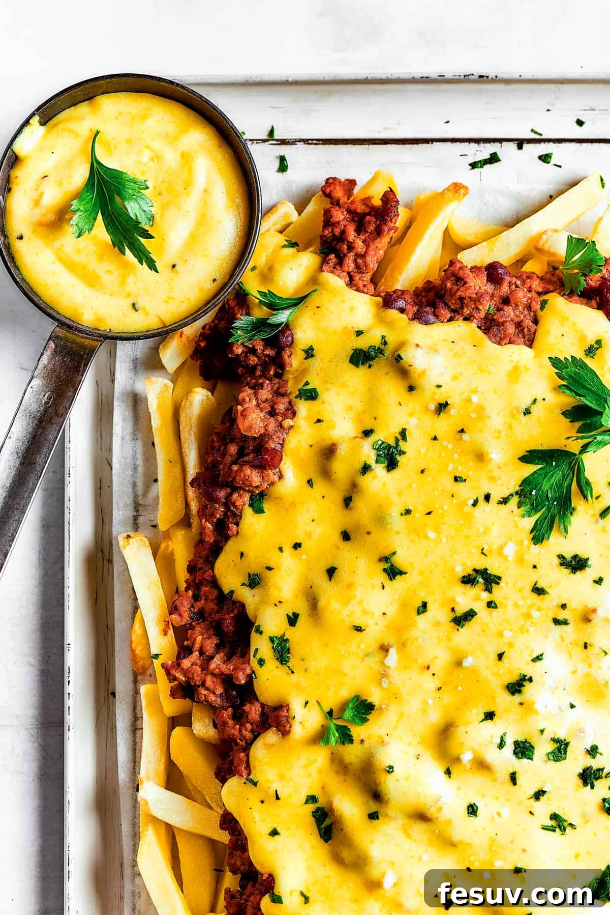 Homemade chili cheese fries with dipping sauce and a blue tea towel.