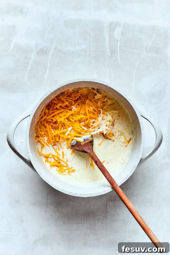 Stirring cheddar cheese into a hot cream mixture to make cheese sauce.
