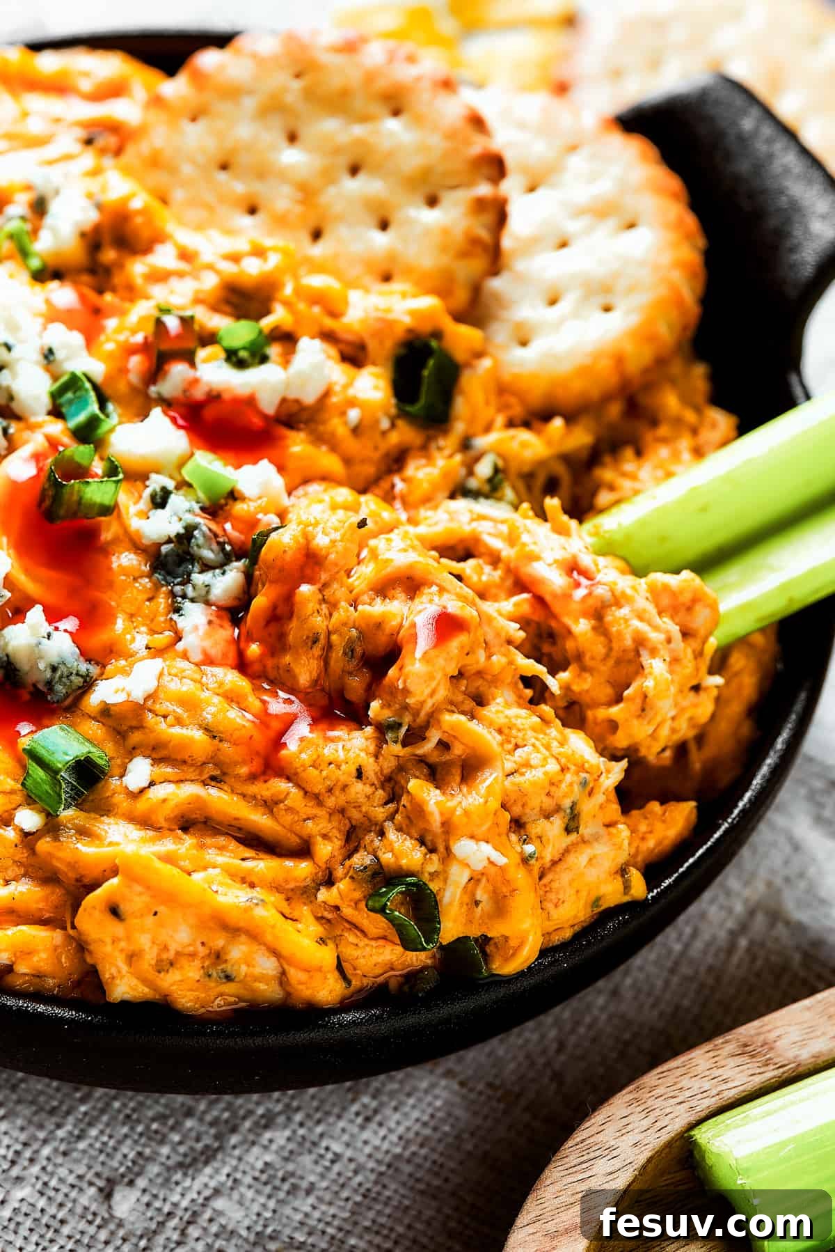 A small, two-handled dish of Crockpot Buffalo Chicken Dip, garnished with fresh celery sticks and crackers, inviting a delightful dip.