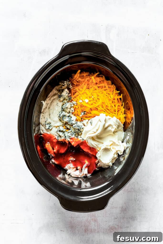 Cream cheese, blue cheese, shredded chicken, and other delicious ingredients nestled in a slow cooker insert, ready to be cooked into a delightful dip.
