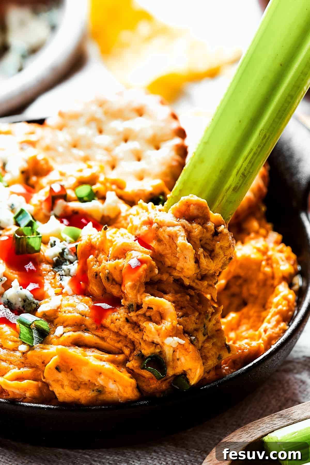 Close-up shot of creamy Crockpot Buffalo Chicken Dip, beautifully garnished with blue cheese crumbles and green onions, with a celery stick poised for dipping.