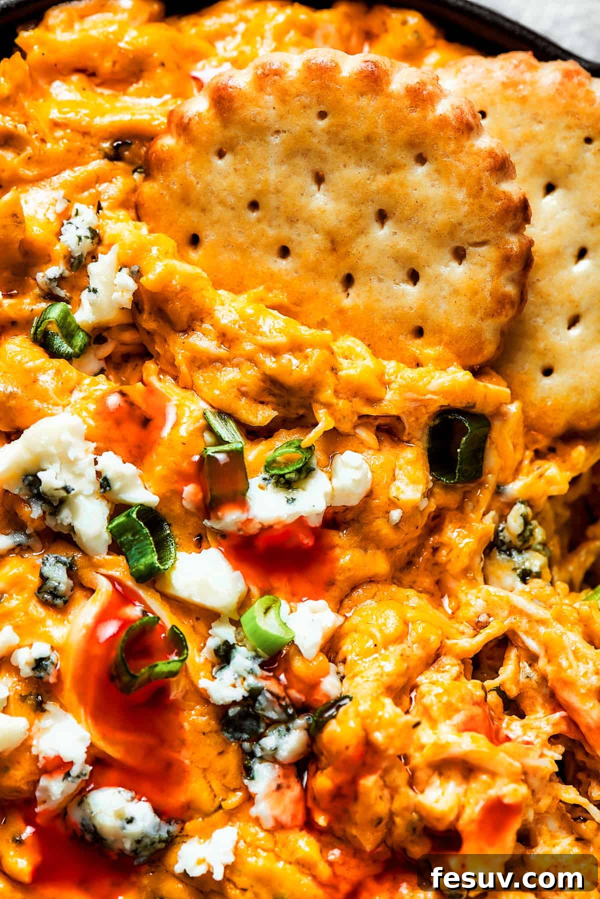 Close-up image of hands gracefully dipping crackers into a warm, inviting dish of Crockpot Buffalo Chicken Dip.