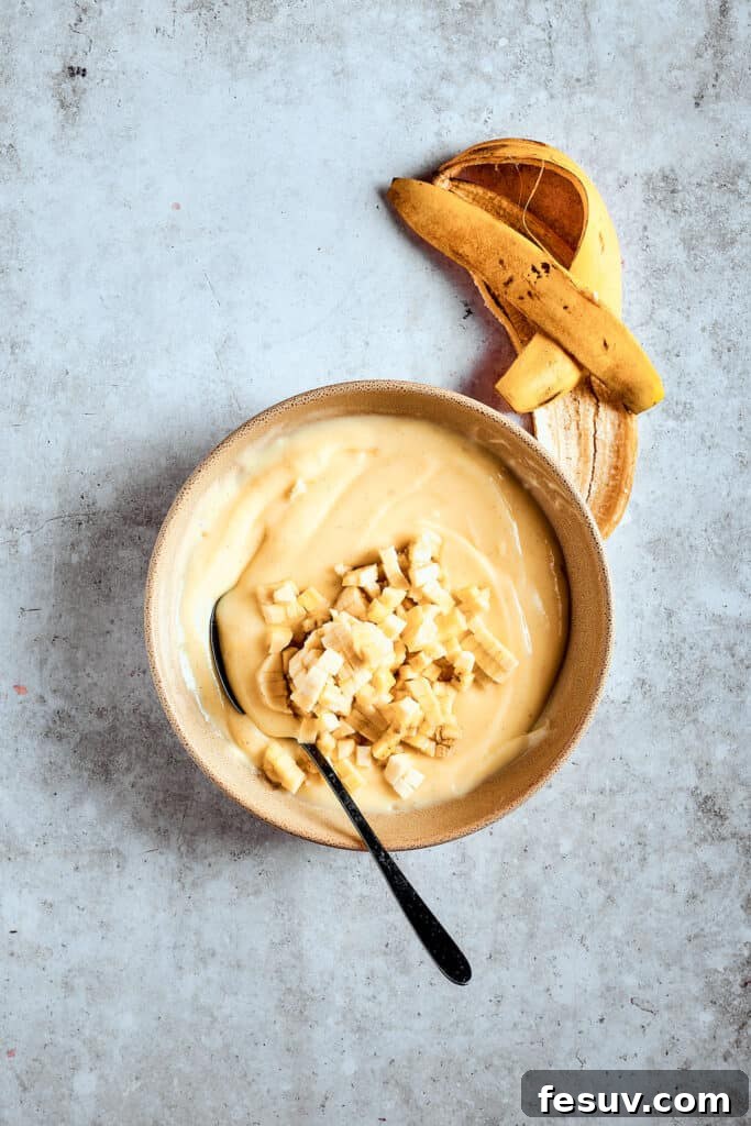Adding bananas ensures flavor in every bite. Chopped bananas being stirred into the creamy banana pudding mixture.