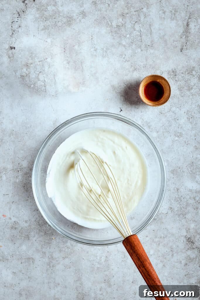 Whip cream until soft peaks form. Whipping heavy cream with vanilla extract in a mixer bowl to create light, fluffy whipped cream.