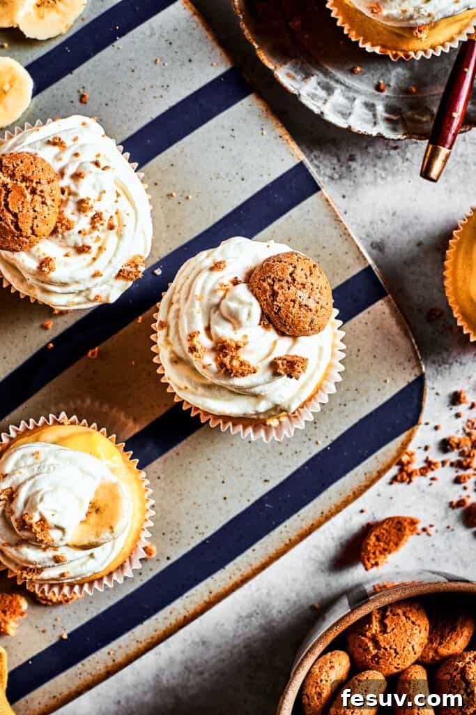 Garnish with fresh bananas and vanilla wafers for the perfect finish. Overhead shot of finished banana pudding cupcakes, garnished with whipped cream, banana slices, and vanilla wafers, arranged on a decorative silver platter.