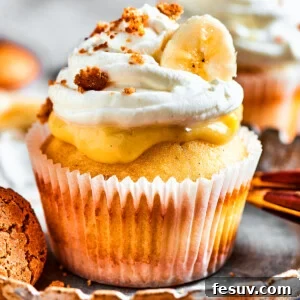 Fluffy cupcakes filled with creamy pudding and topped with perfect banana pudding garnishes. One banana pudding cupcake on a dessert plate with more in the background.