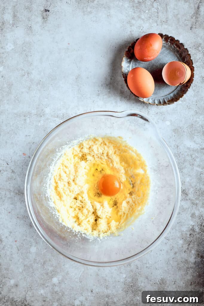 Adding eggs gradually ensures a smooth batter. Adding eggs one by one to the creamed butter and sugar mixture.