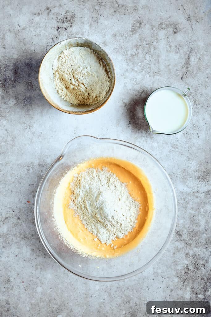 Alternating dry and wet ingredients for perfect batter. Gradually adding dry ingredients to the cupcake batter in a mixing bowl.