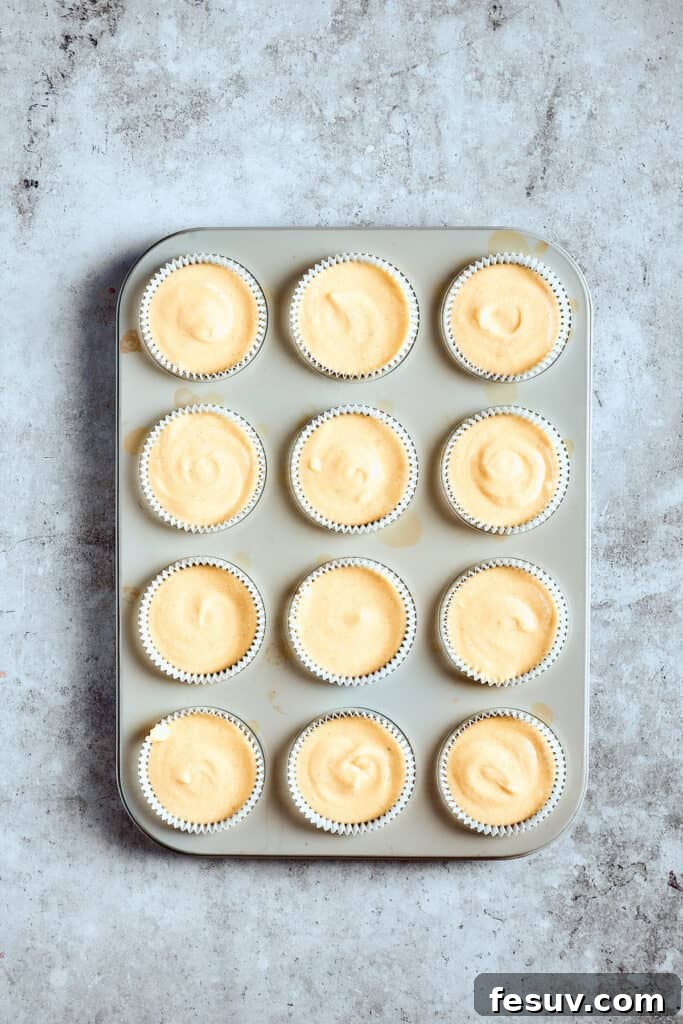 Fill cupcake liners two-thirds full for best rise. Unbaked cupcake batter in liners, placed in a cupcake pan, ready for the oven.