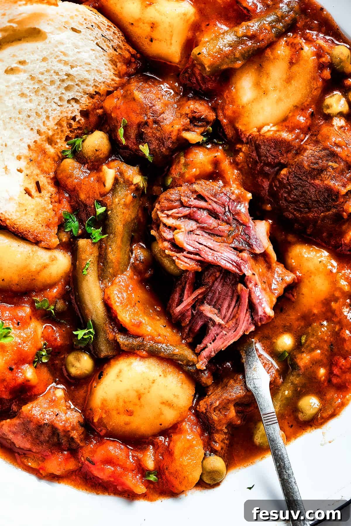 As the air gets crisper and the leaves turn golden, it's time to cozy up with a bowl of pure comfort - this old-fashioned Mulligan Stew! Close-up shot of a piece of white bread dipped in Mulligan stew.