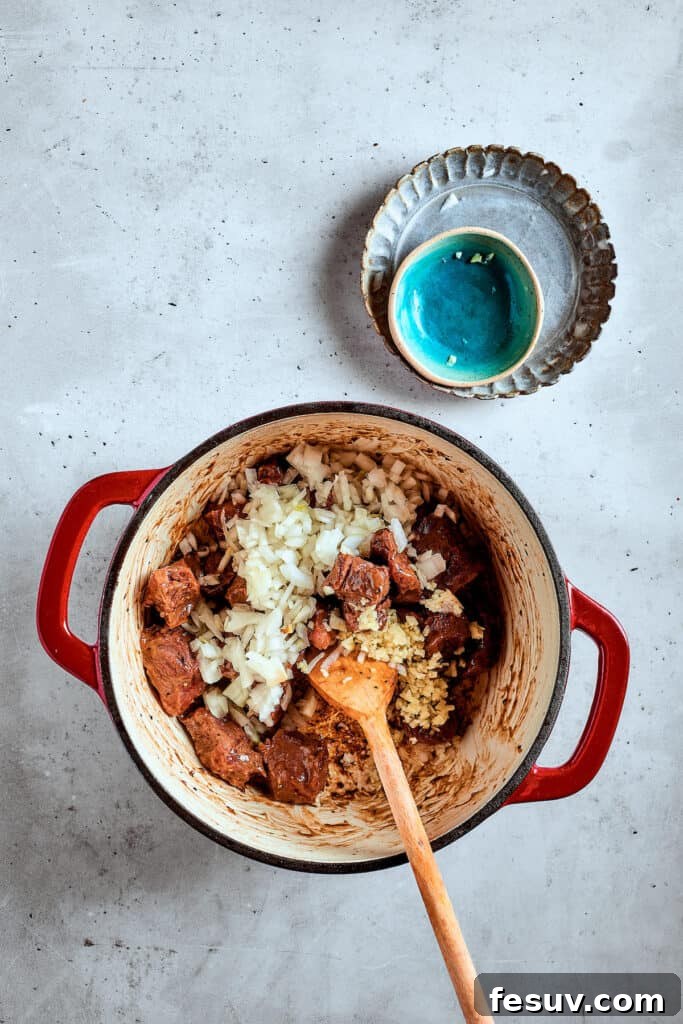 As the air gets crisper and the leaves turn golden, it's time to cozy up with a bowl of pure comfort - this old-fashioned Mulligan Stew! Adding onion and garlic to a pot of browned beef.