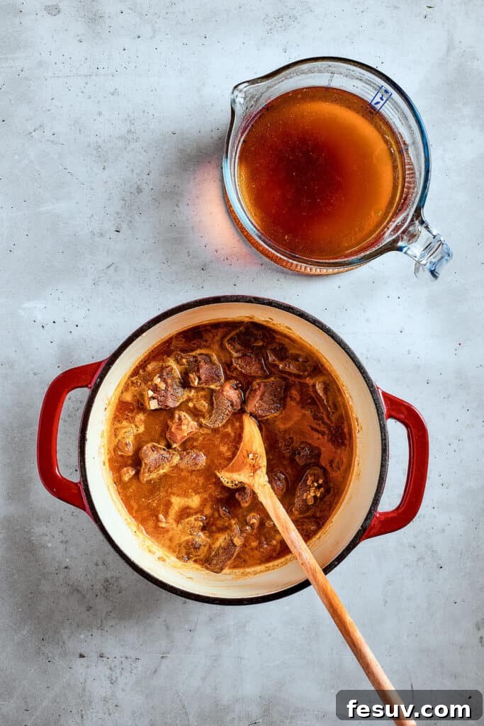 As the air gets crisper and the leaves turn golden, it's time to cozy up with a bowl of pure comfort - this old-fashioned Mulligan Stew! Pouring broth over chunks of beef in a pot.